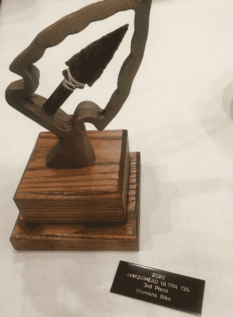 Downward view of Trophy with arrowhead on wood base with an Arrowhead Ultra 135 third place plague next to it on a table