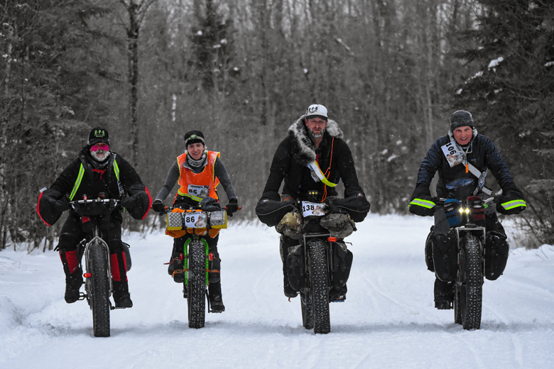 Front view of four winter cyclists riding fat bikes on snow covered  trail in the woods