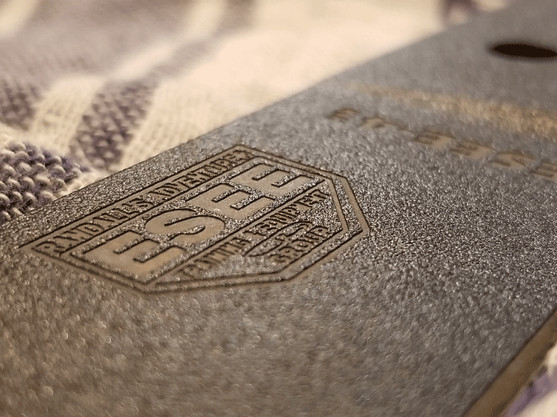 Angled close up of a portion of a black powder coated knife blade with an ESEE logo lying on woven blanket