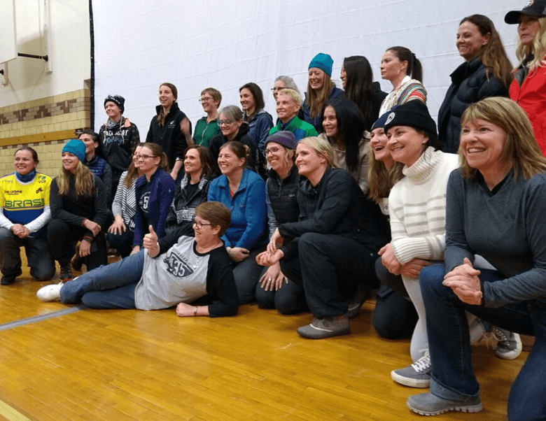 Angled view of a group of smiling bike race participants pose for a picture in a gymnasium 