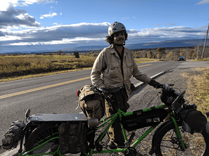 Right side view of a green Surly Big Dummy bike, on the shoulder of a paved highway, with a cyclist standing behind